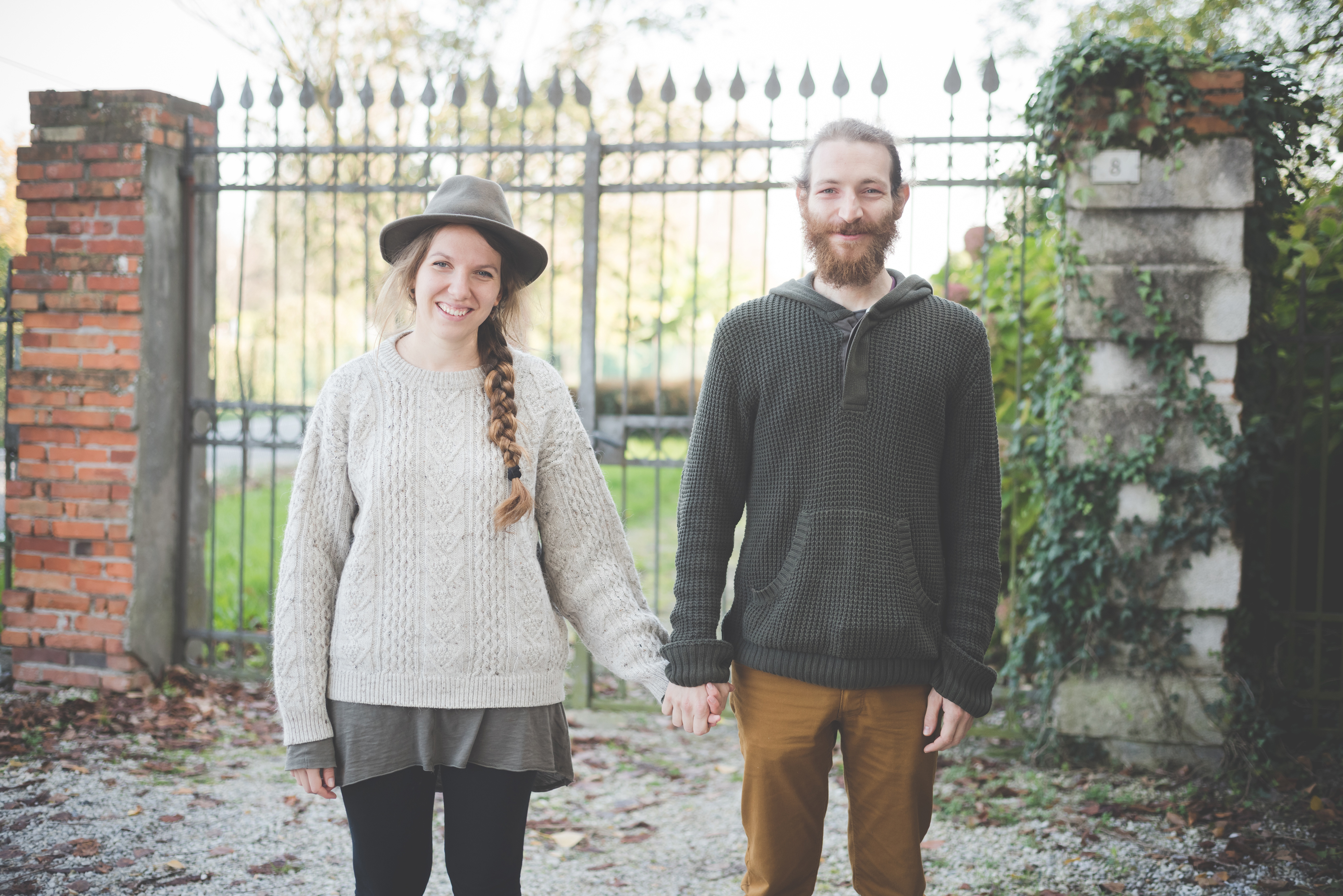 couple holding hands, brick gate, gate, metal gate, wrought iron gate, cute couple, happy couple, hat, braid, layered clothes, men's hoody, sweater season, fall style,