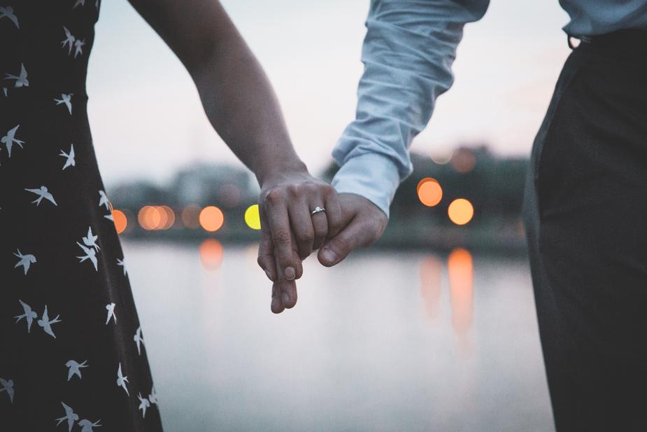 happy couple, wedding ring, engagement ring, diamond ring, couple holding hands, lake, water, reflections on water, black dress, white bird dress, patterned dress, business clothes, evening, sundown