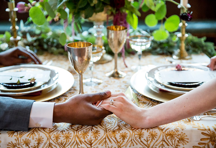 couple holding hands, wedding ring, diamond ring, engagement ring, bridal set, plates, wedding dinner, bride and groom, metal chalice, metal goblets, exotic wedding, gold tablecloth, gold and ivory, gold candlesticks, wedding table, wedding centerpiece, biracial couple, exotic wedding decor, eco chic wedding, boho wedding style,