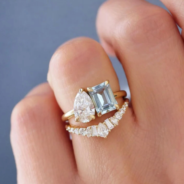 pear shaped diamond and emerald aquamarine two-stone engagement ring with curved diamond band
