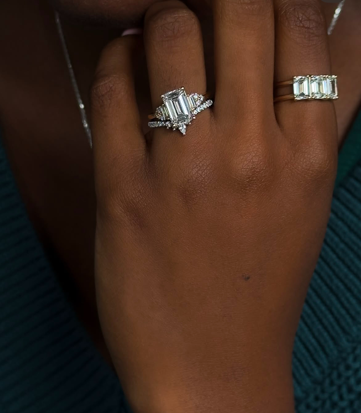 black woman's hand with large emerald cut diamond engagement ring and chevron style band. Three stone luxe band