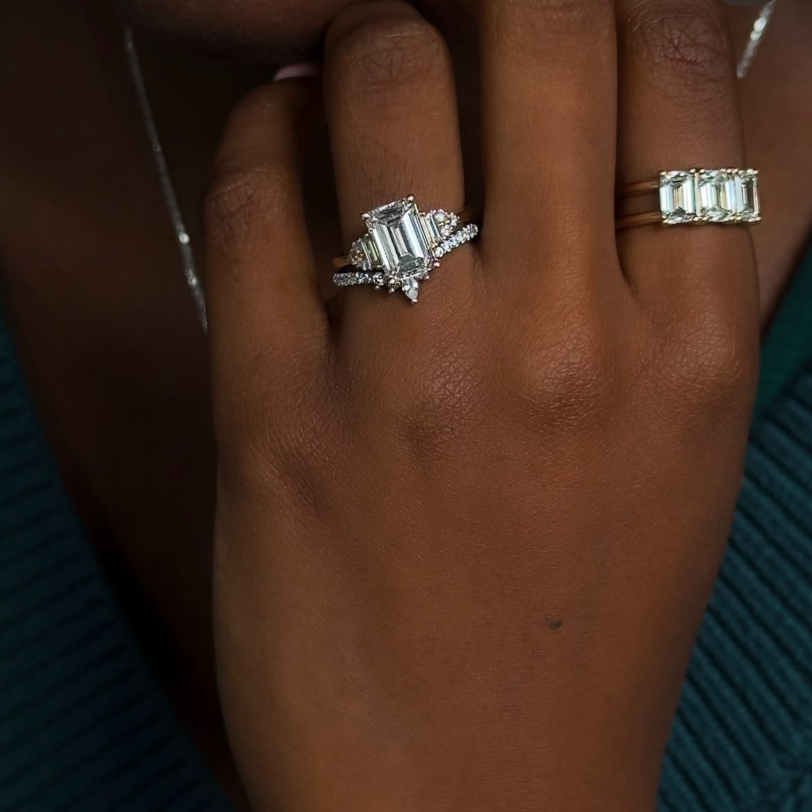 Black woman'd hand with elongated diamond engagement ring and luxe three-stone band